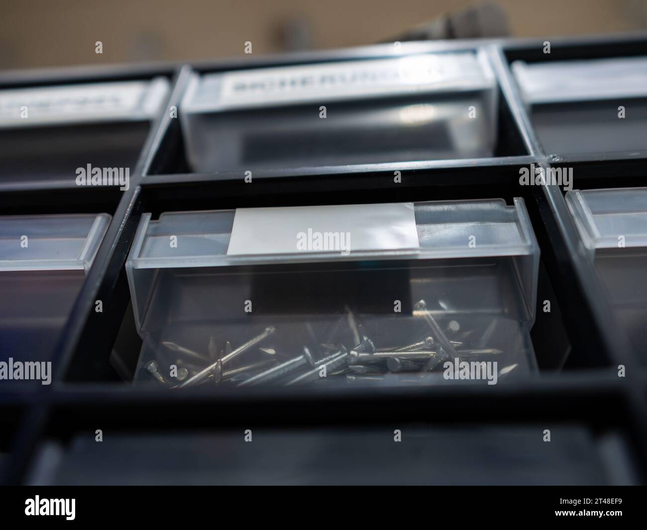 Plastic bin with small nails in a storage box. The label is empty. The hardware in a garage workshop is organized in different compartments. Stock Photo
