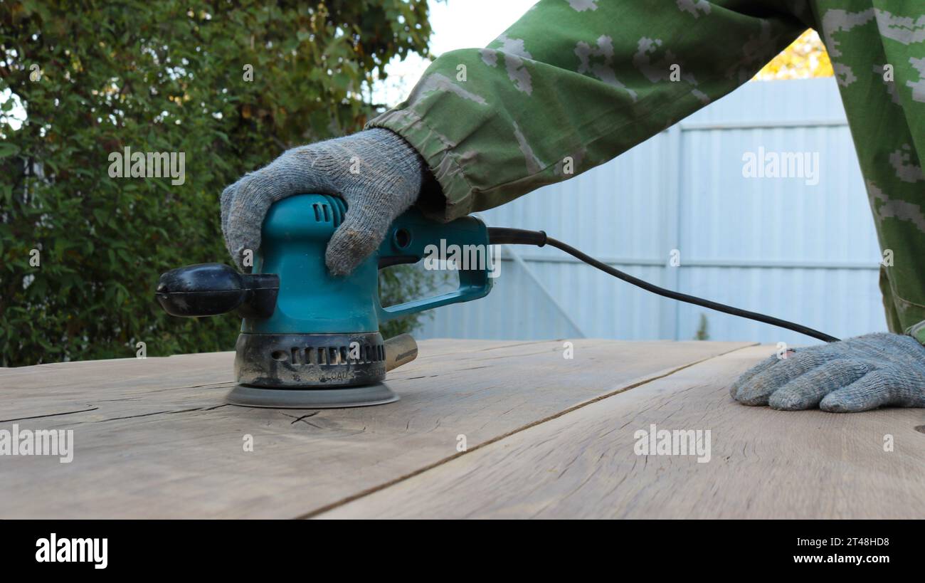 carpenter's hands holding a sander and polishing the surface of