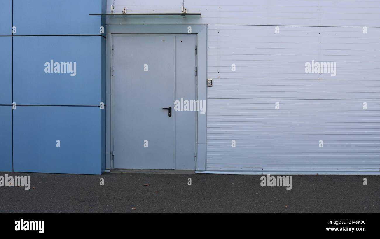 wall of a building made of gray and blue panels with a closed door as an urban abstract texture background with copy space, a side exit from a store Stock Photo