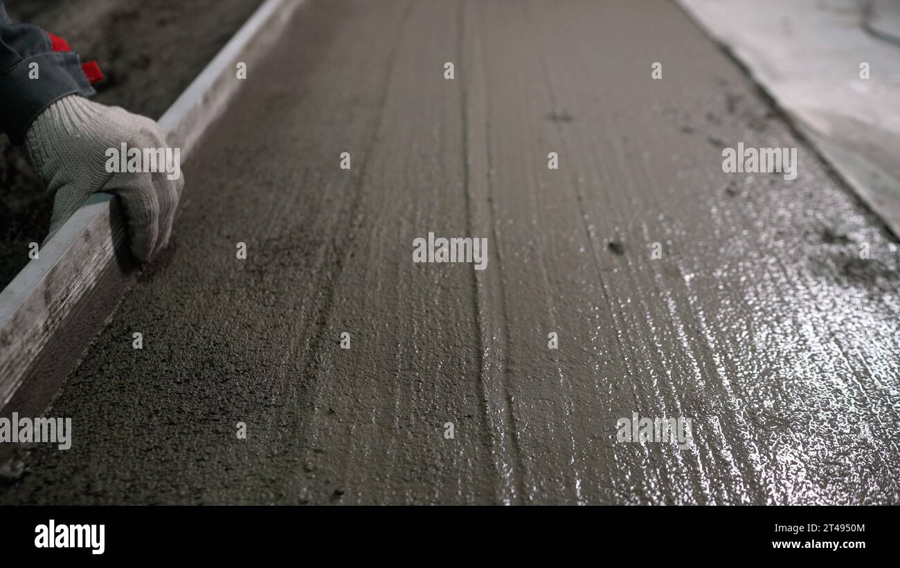 A builder uses a trowel to level a cement mortar screed. Concrete work on a construction site