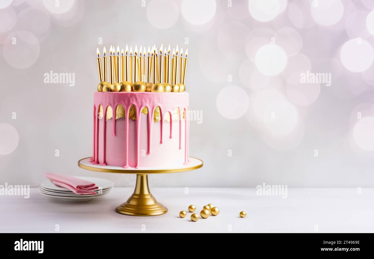 Pink birthday cake decorated with gold drip icing, gold leaf and lots of gold birthday candles Stock Photo