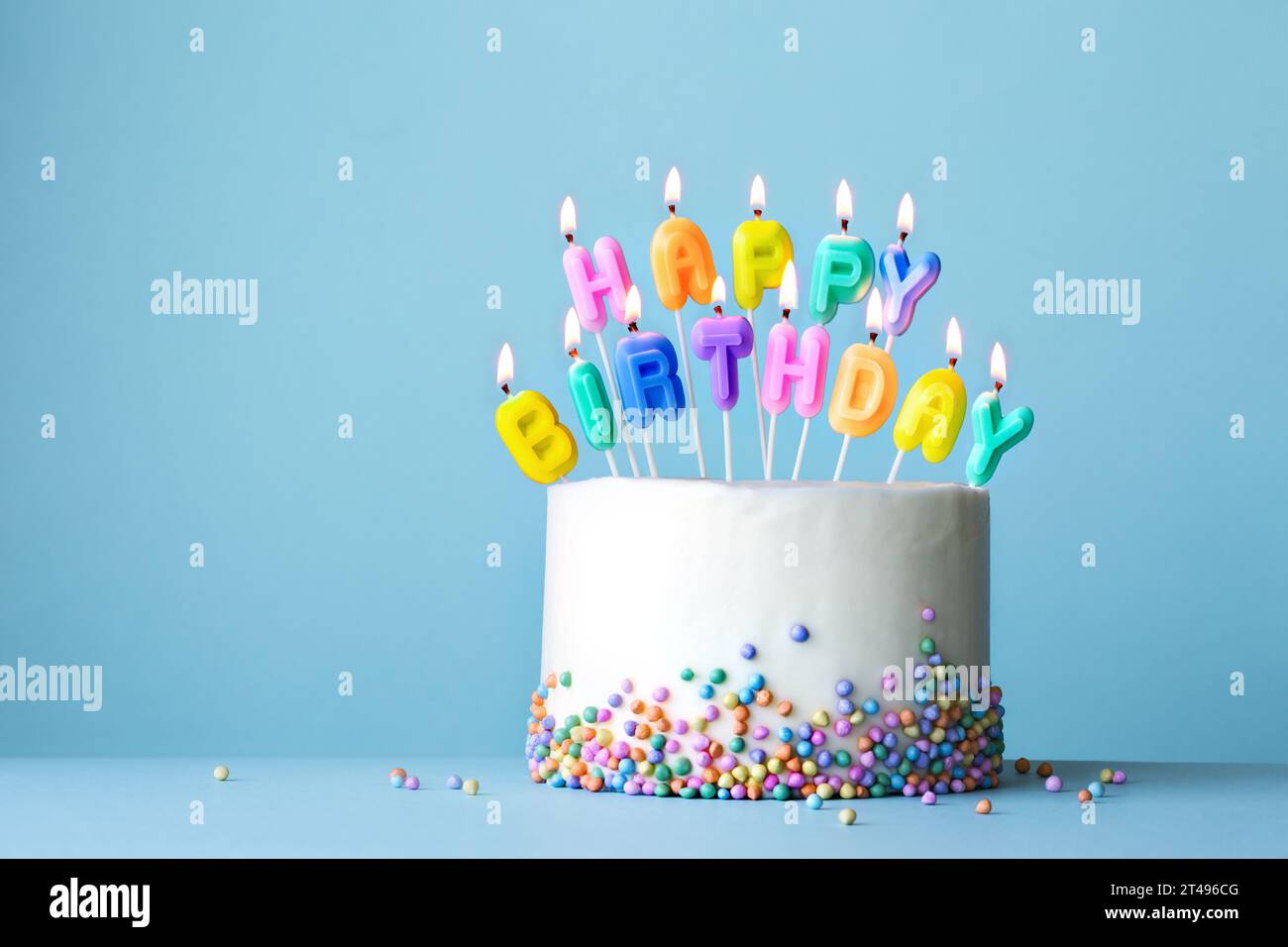 Colorful birthday cake with birthday candles spelling happy birthday against a blue background Stock Photo