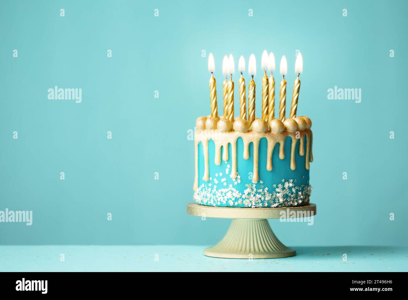 Elegant turquoise birthday cake with gold drip icing and gold birthday candles against a turquoise background Stock Photo