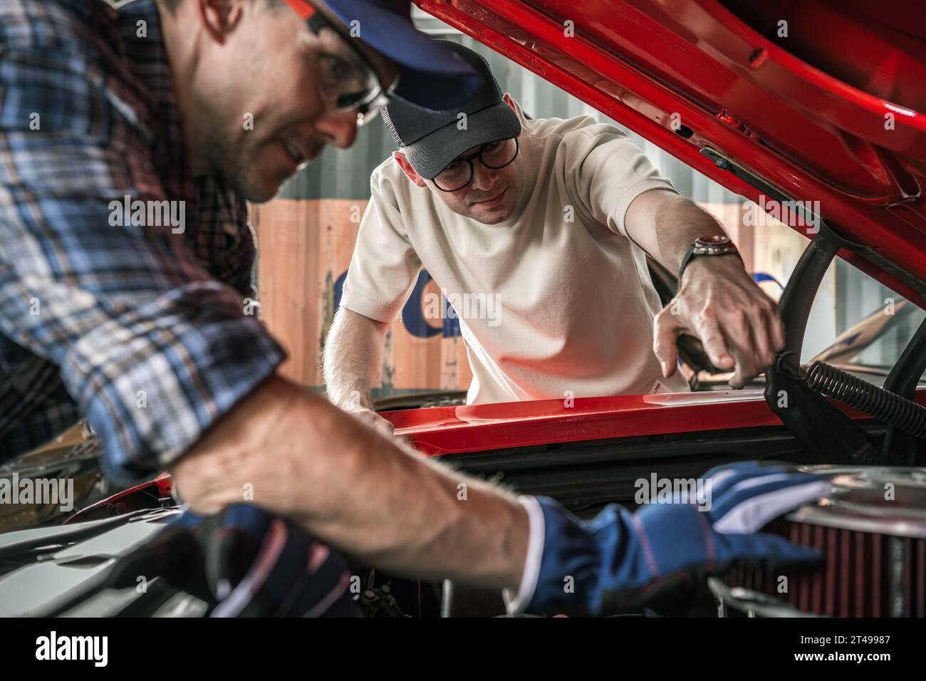 Two Caucasian Classic Muscle Cars Enthusiasts Working on the Car Engine