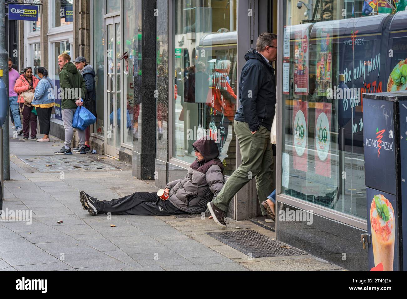A homeless man sits in front of the shop on the street waiting for