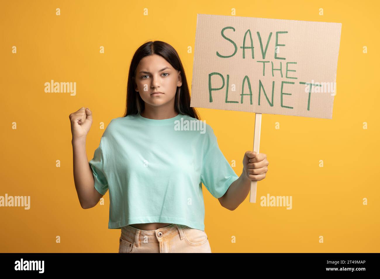 Serious confident brunette teen girl showing holding save the planet poster on yellow background. Stock Photo