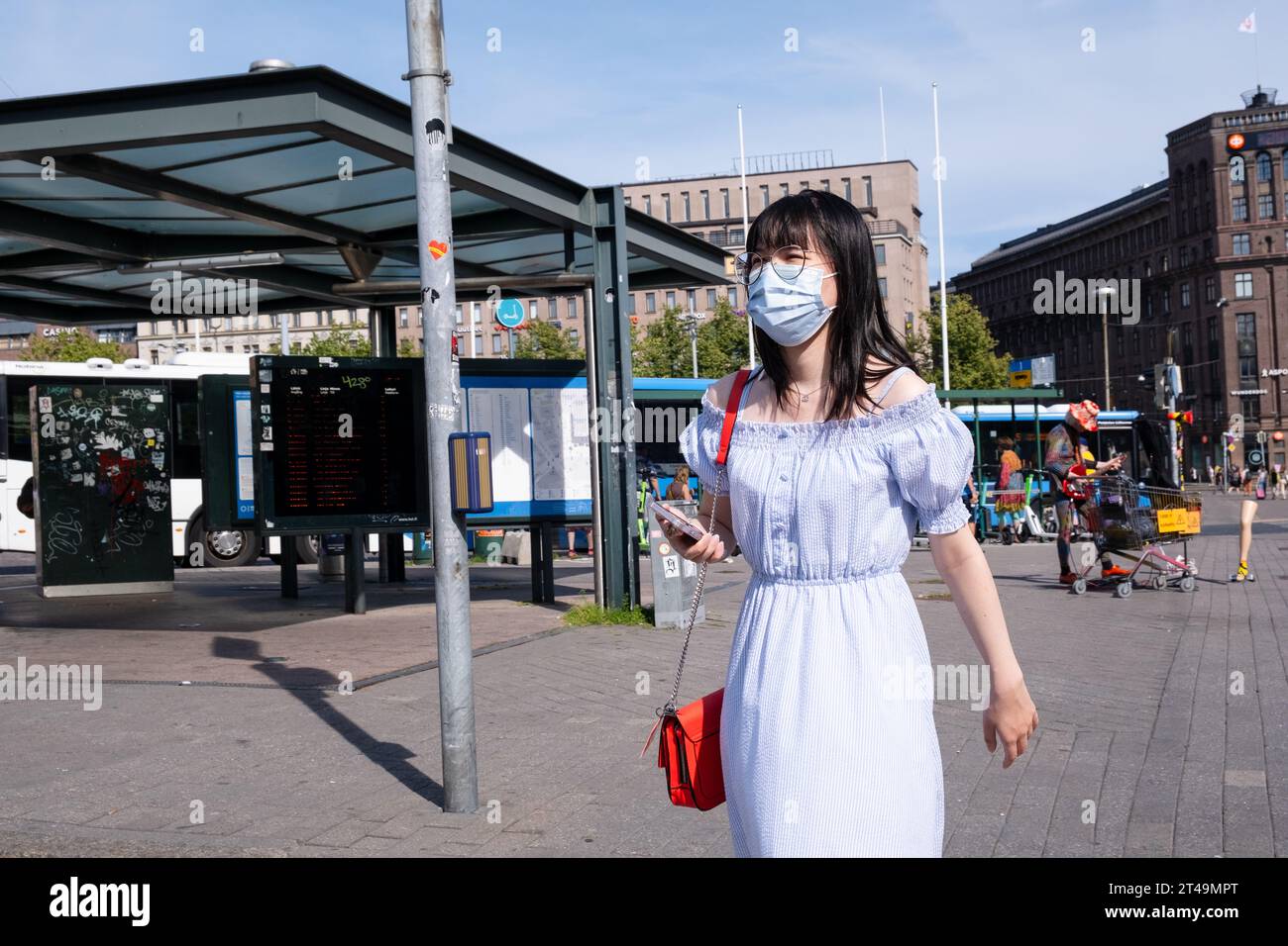 A pedestrian in a facemask with a mobile phone in a white summer dress ...