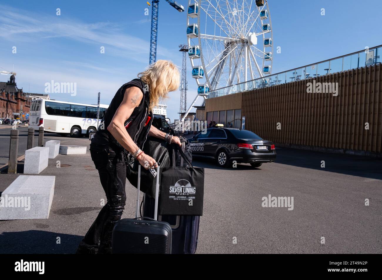 Finnish heavy metal icon Michael Monroe from Hanoi Rocks exits a taxi with suitcases and a vinyl record bag in summer in central Helsinki, Finland. Stock Photo