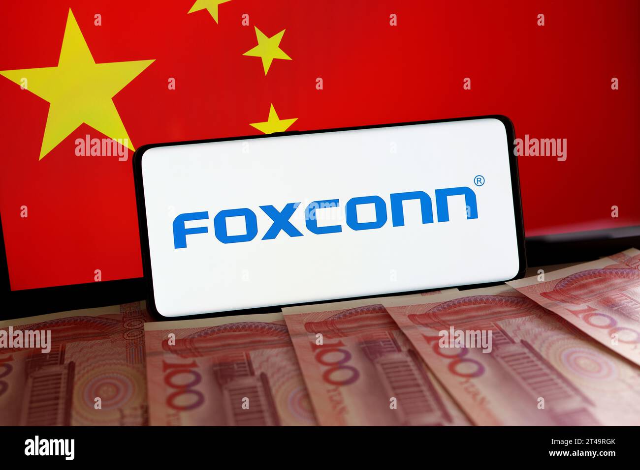 Iphone manufacturer  FOXCONN logo on smartphone, Yuan banknotes and blurred flag of China at the background screen. Concept. Stafford, United Kingdom, Stock Photo