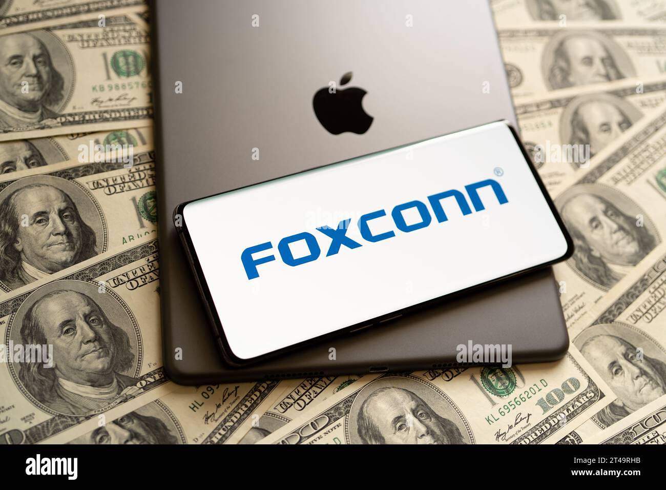 FOXCONN logo seen on smartphone, Apple logo seen on IPad and US dollar bills around. Concept. Stafford, United Kingdom, October 29, 2023 Stock Photo