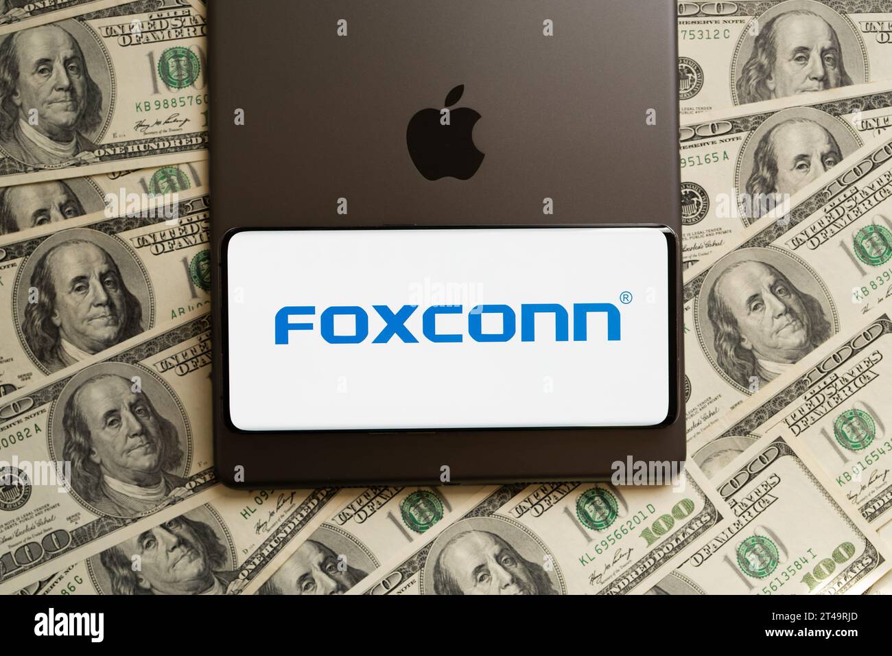 FOXCONN logo seen on smartphone, Apple logo seen on IPad and US dollar bills around. Concept. Stafford, United Kingdom, October 29, 2023 Stock Photo