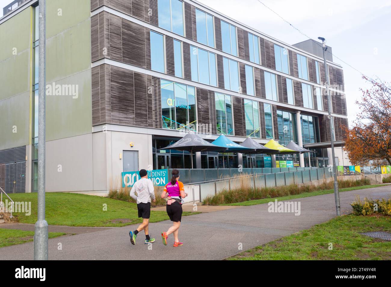 Rear side view of joggers running past ARU Student Union building , Anglia Ruskin University, Chelmsford, Essex Campus, Britain, UK. Stock Photo