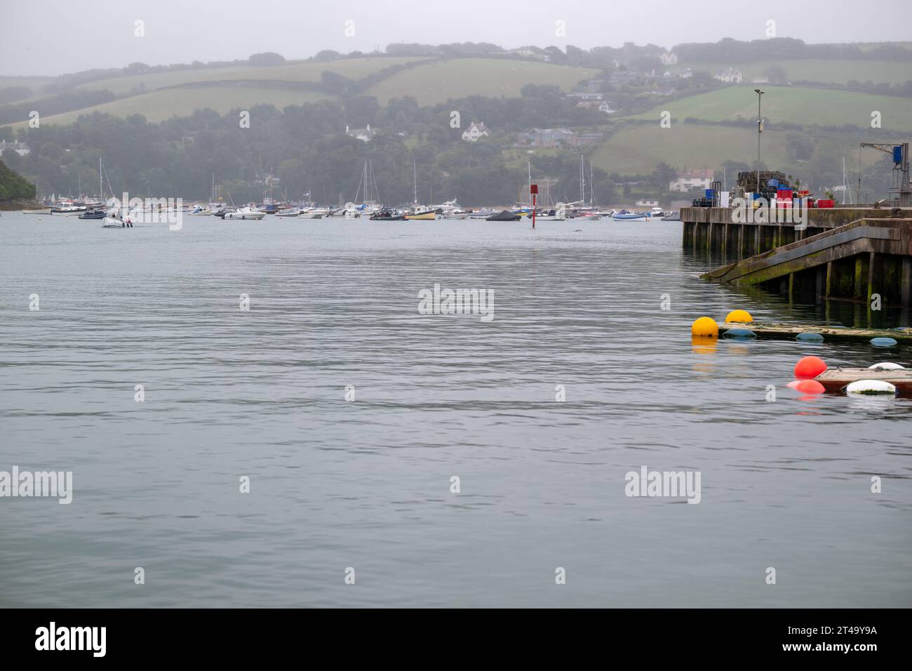View of East Portlemouth across Salcome Estuary taken from the Harbour on misty summers day, with bouys in the foreground and moored boats in distance Stock Photo