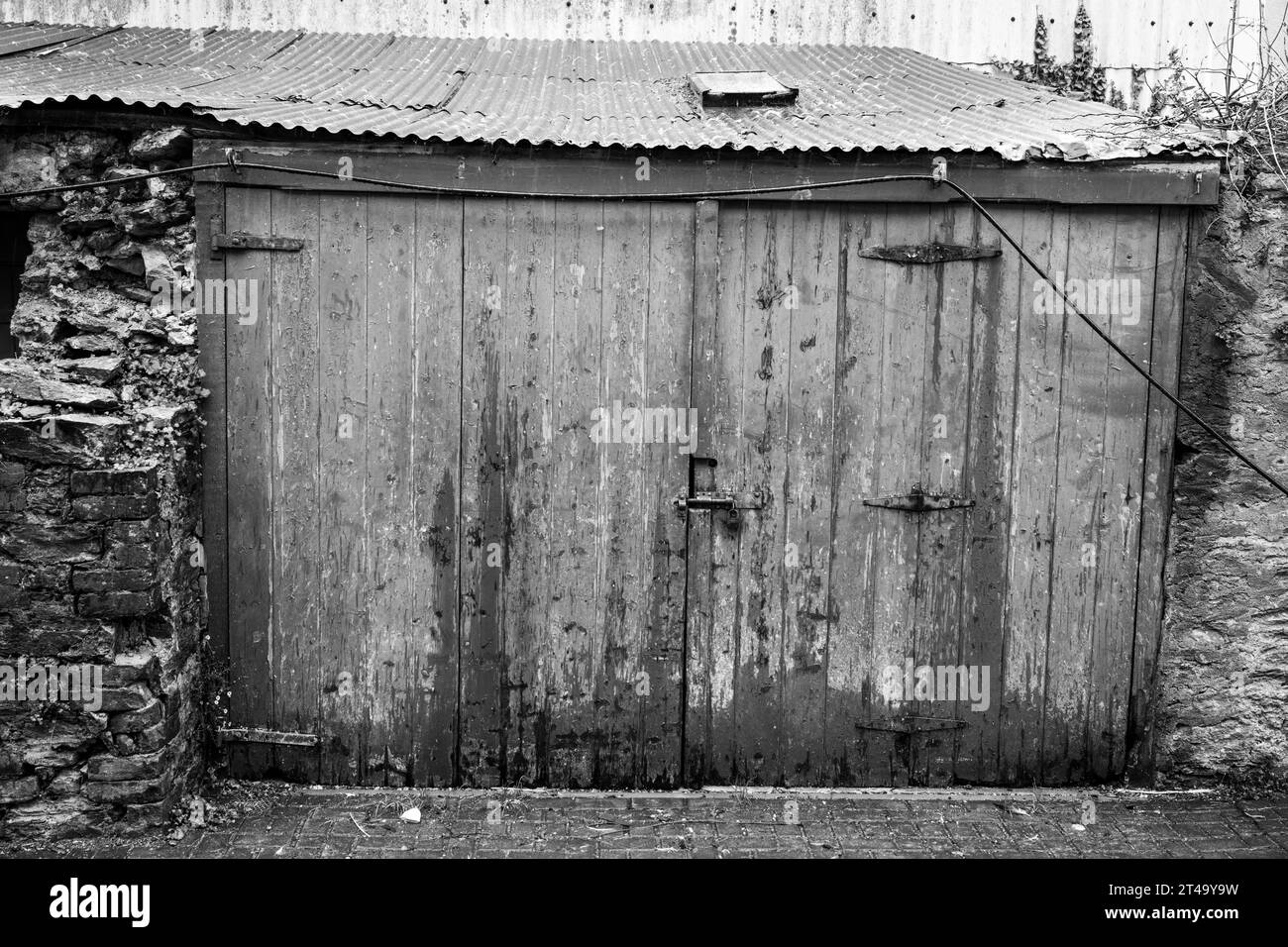 Ramshackle shed, shot in black and white, with vertical wood panelled doors between stone walls, found just off Island Street, Salcombe. Stock Photo