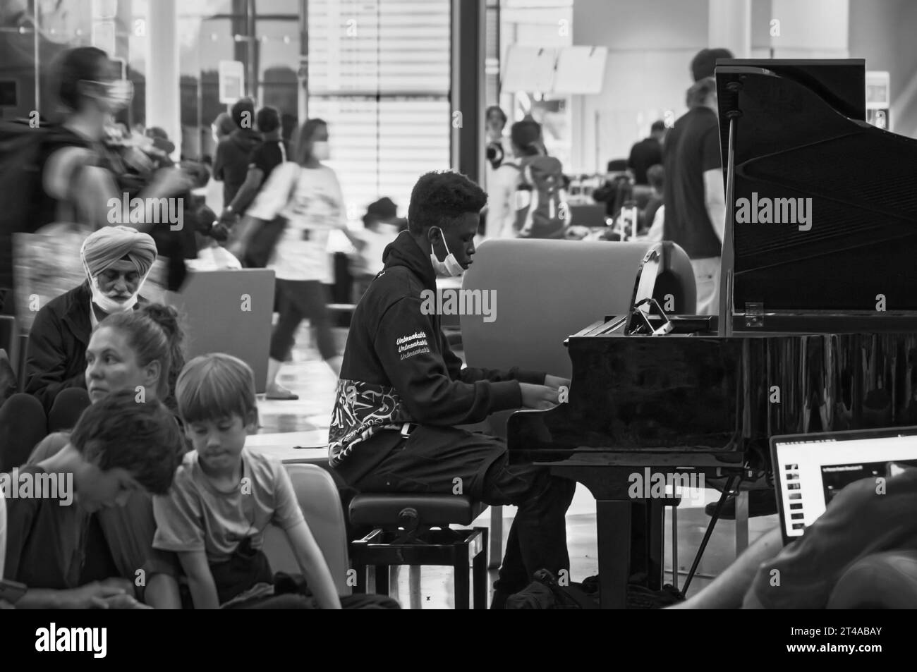 Montreal, Quebec, Canada - 07 04 2022: A teenage musician wearing black Unbreakable hoodie playing black grand piano amid crowded busy outbound Stock Photo