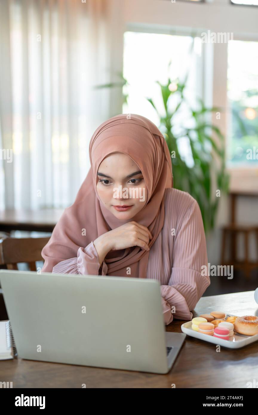 A concentrated and serious Asian-Muslim woman in a hijab is looking at ...