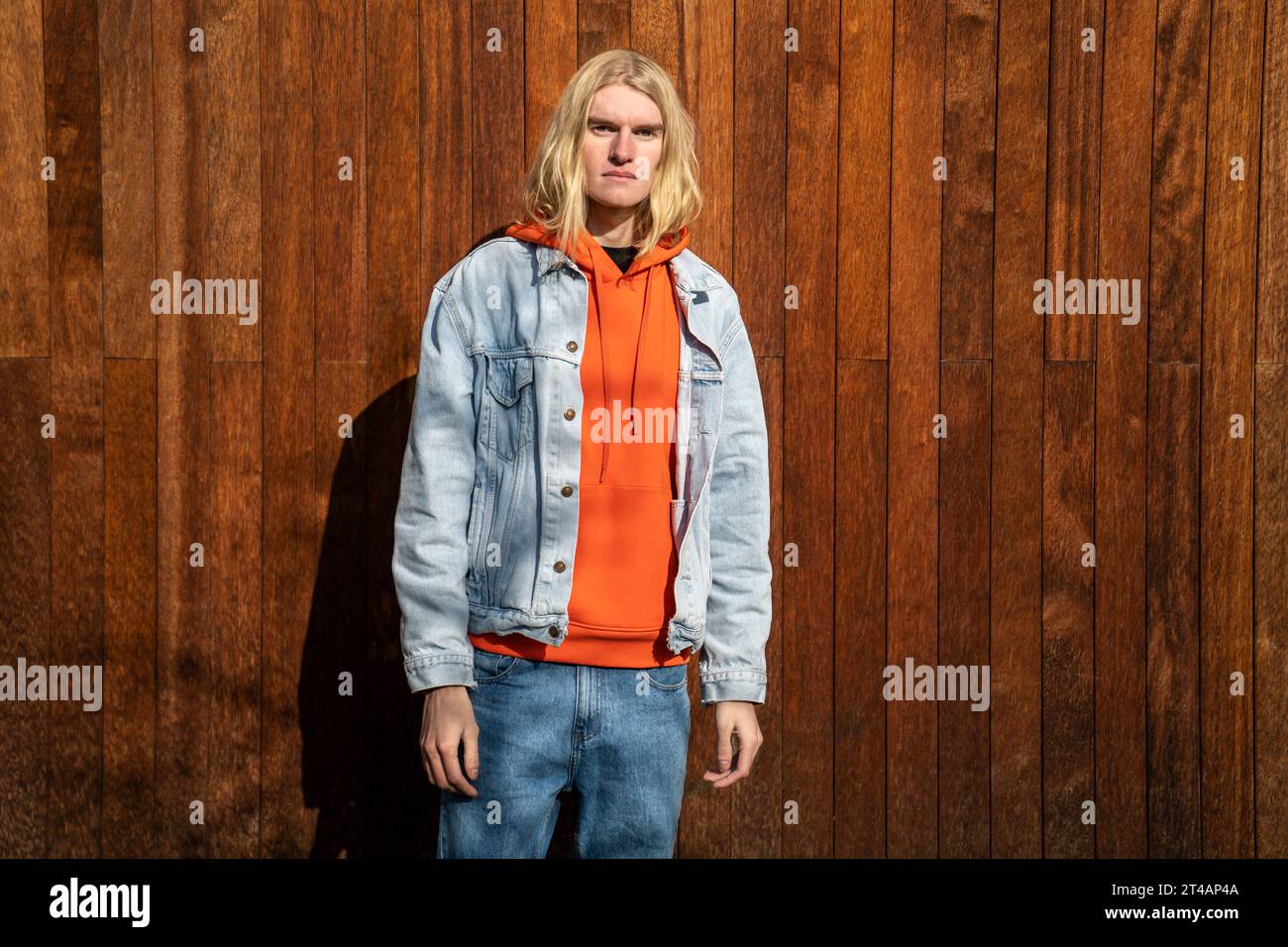 Apathetic blond long hair man scandinavian androgynous appearance stands near wooden fence. Stock Photo