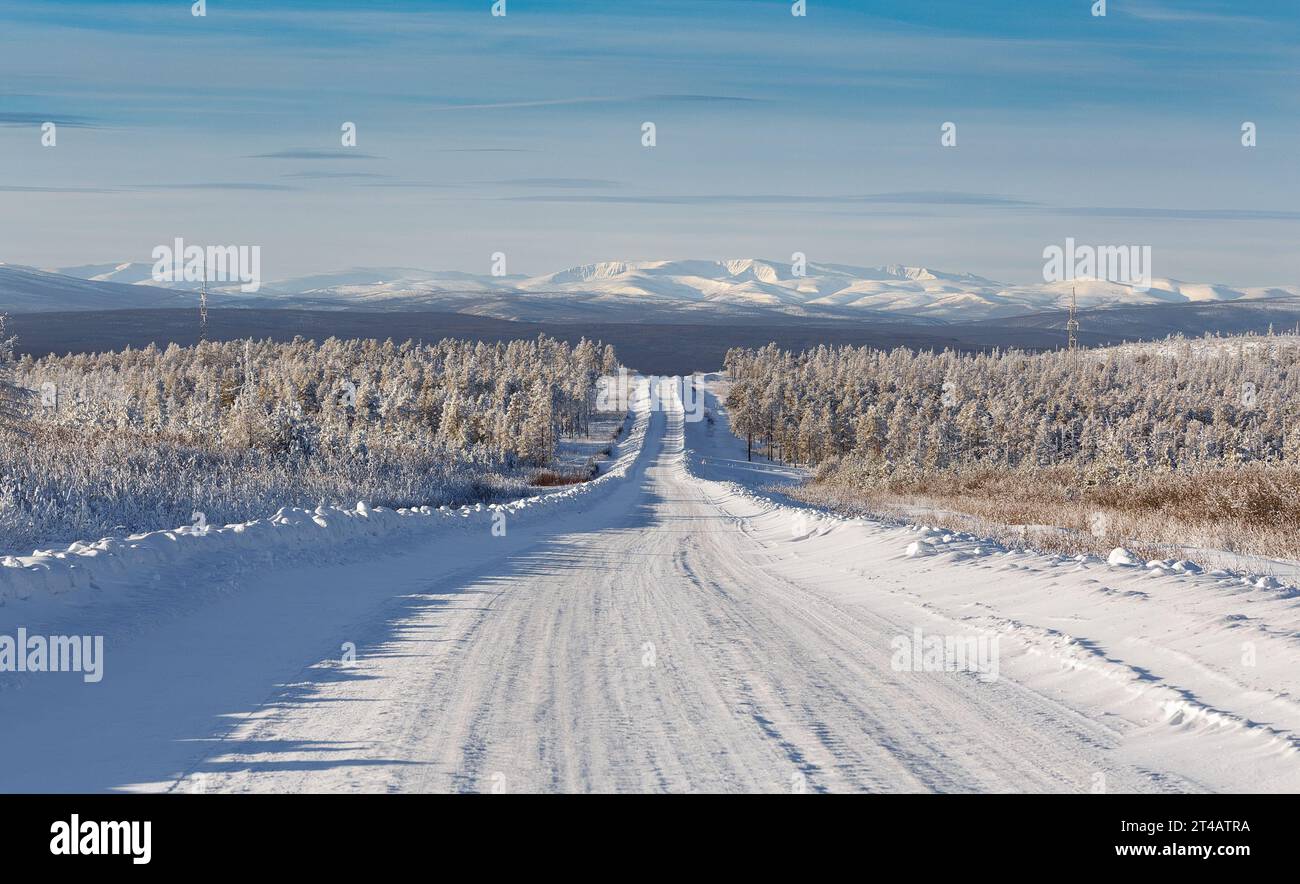 Winter road going down the slope of the hill against the backdrop of the Zverev ridge in South Yakutia, Russia Stock Photo