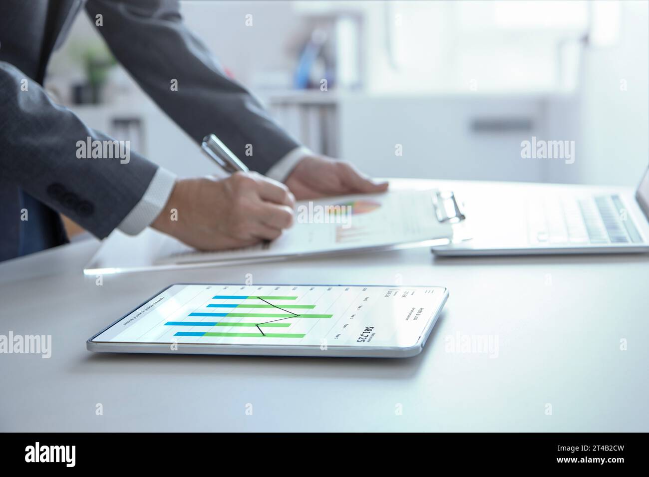 Businessman standing in the office reviewing financial annual reports with modern tablet and laptop computer for a return on investment. Stock Photo
