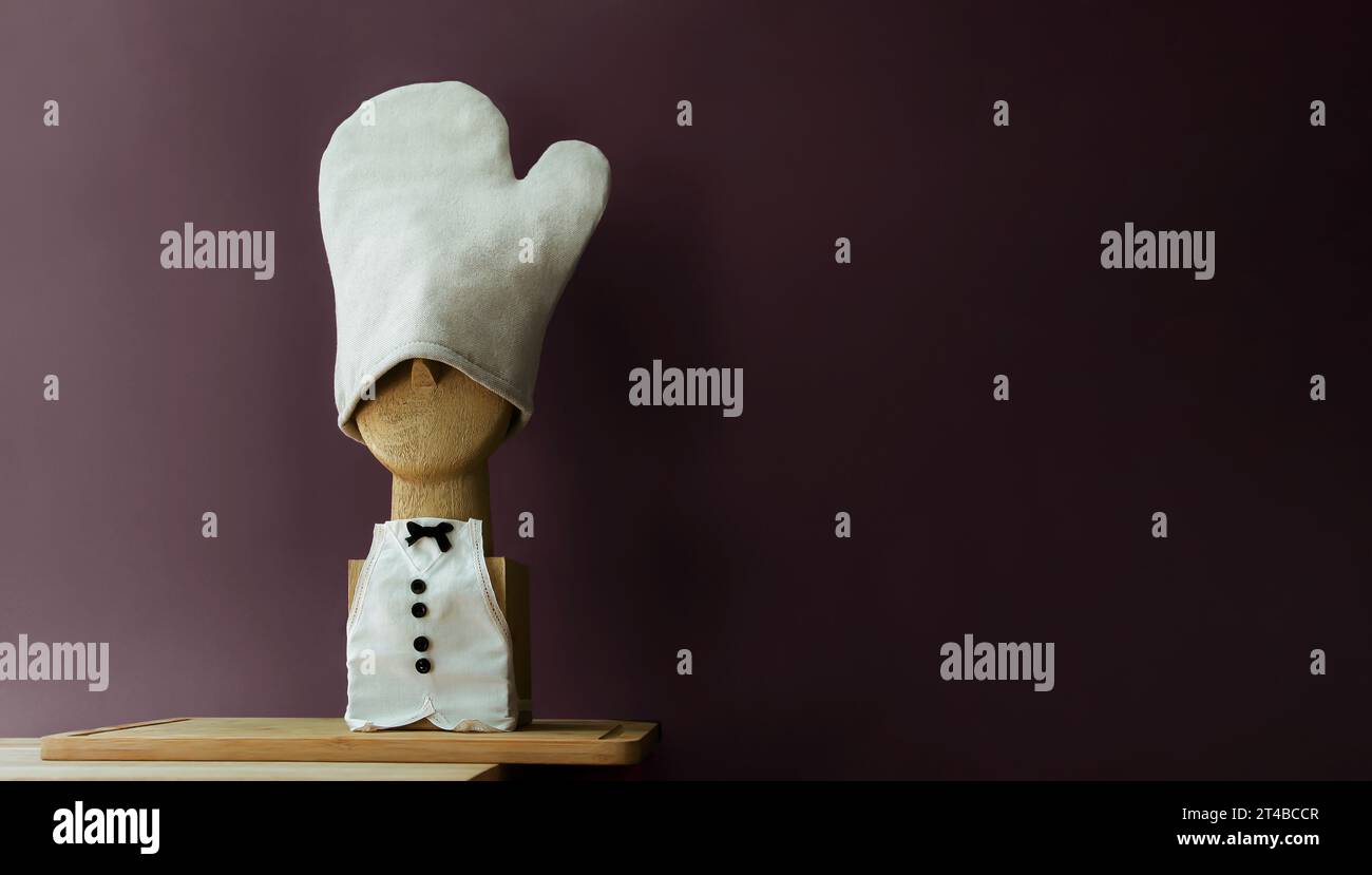 Exclusive funny horizontal composition of the wooden chef's bust on the wooden cutting board. Bow tie frog. Miniature apron and kitchen glove Stock Photo