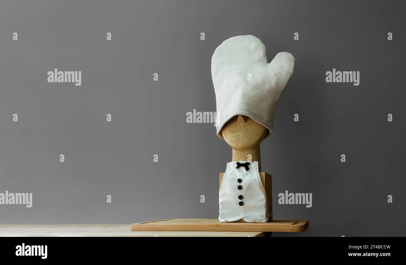 Exclusive funny horizontal composition of the wooden chef's bust on the wooden cutting board. Bow tie frog. Miniature apron and kitchen glove Stock Photo