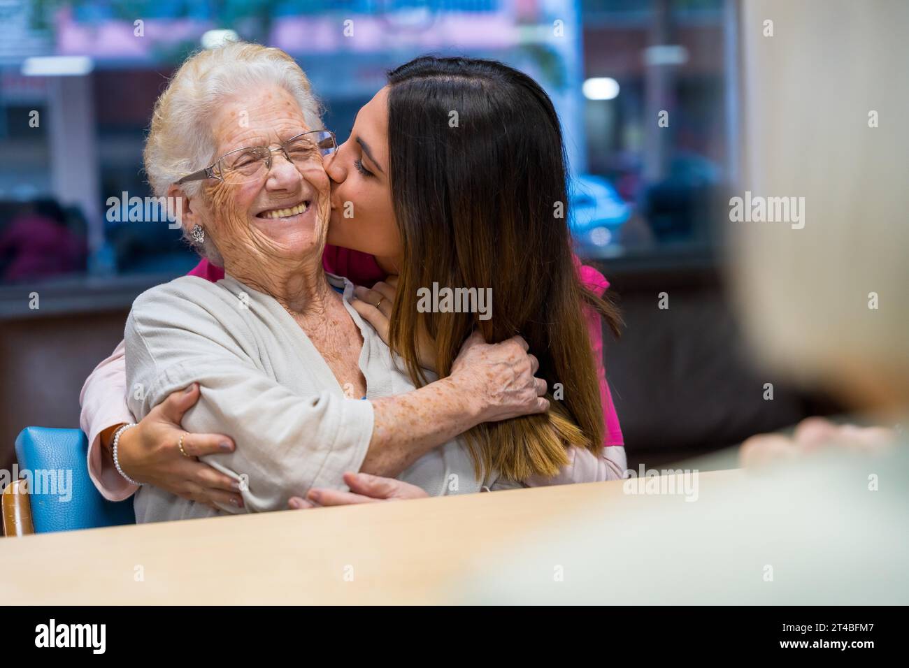 Happy moment of an elder woman and nurse embracing and kissing in a geriatric Stock Photo