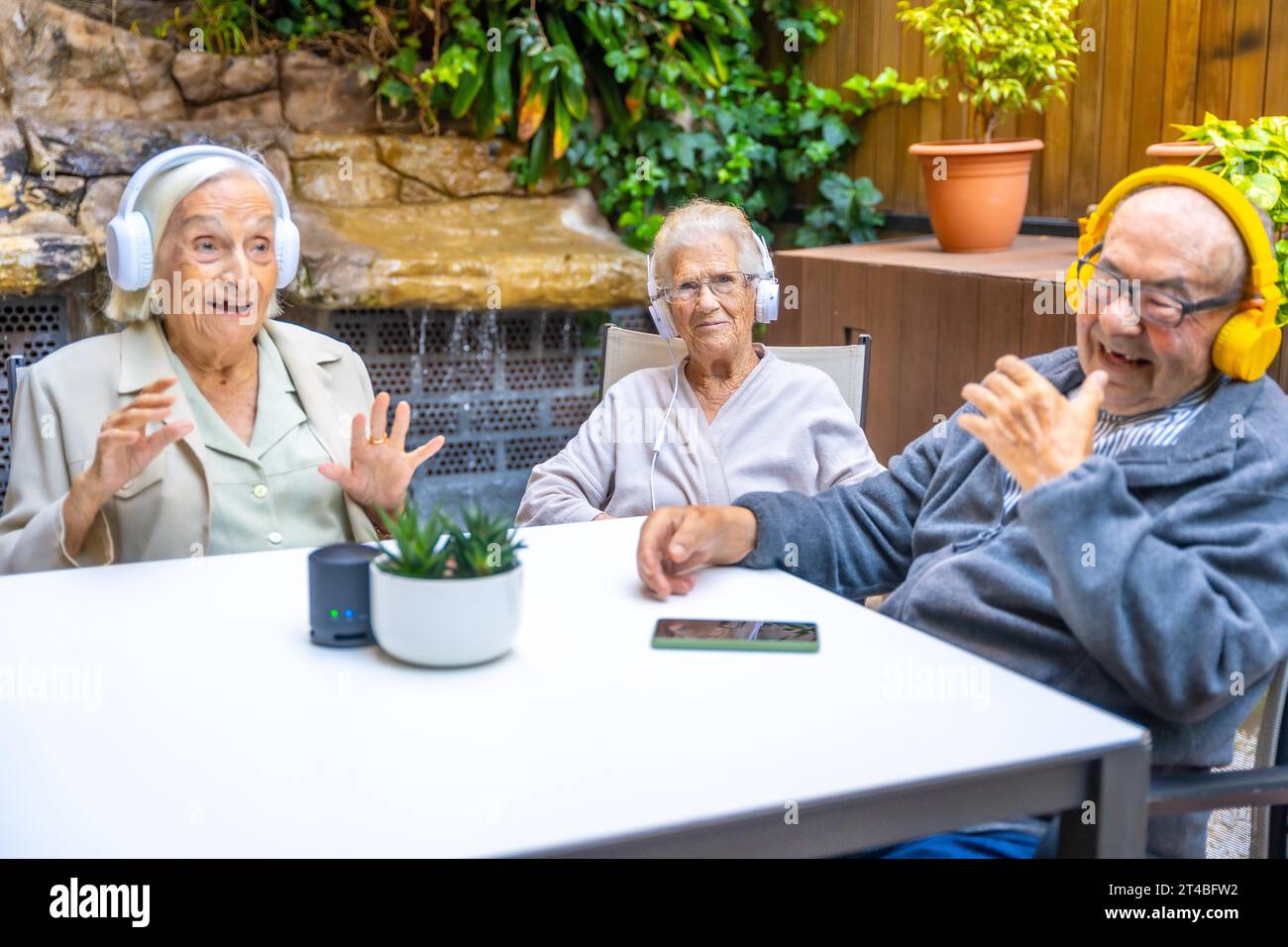 Three happy and cute seniors enjoying listening to music with headphones in a geriatric Stock Photo