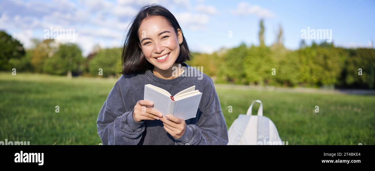 Beautiful woman sitting in park with book. Smiling asian girl reading ...