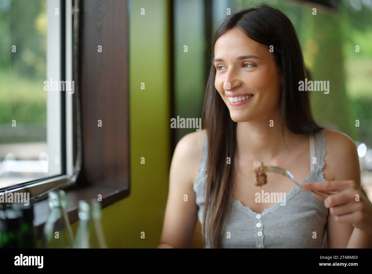 Happy woman in a restaurant eating meat looking through a window Stock ...