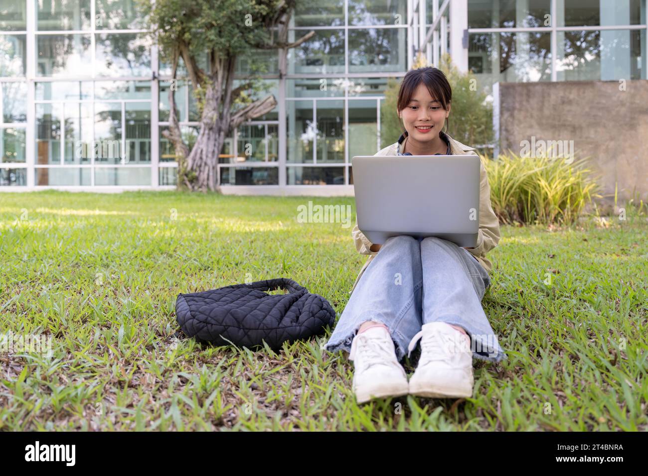 Happy asian female student sitting on lawn, with laptop, beautiful ...