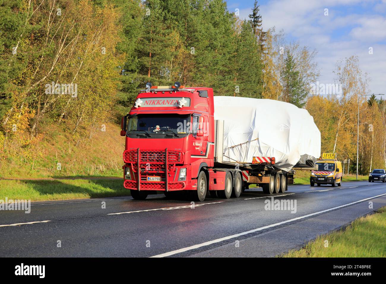 Red Volvo FH truck flatbed trailer M Nikkanen Ky hauls wide load. The transport has 3 pilot vehicles front and back. Raasepori, Finland. Oct 13, 23 Stock Photo