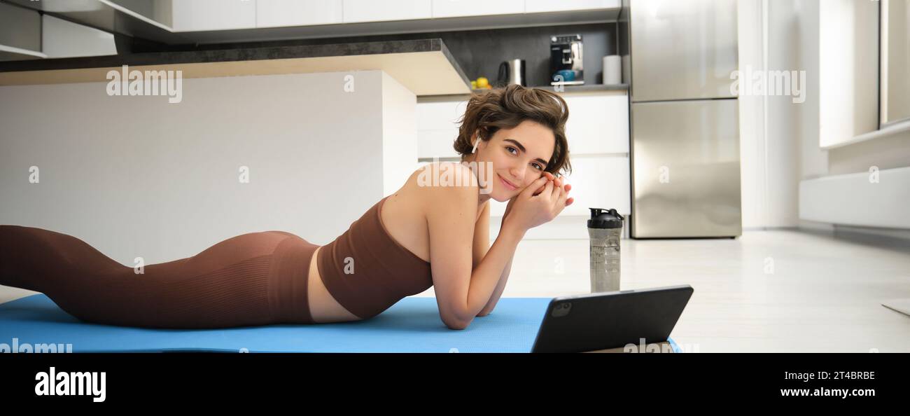 Young fitness instructor, woman does yoga, looks at tablet