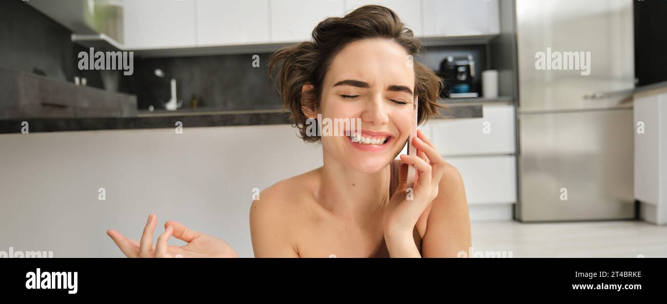 Close up portrait of happy smiling woman talking on mobile phone from her kitchen. Chatty girl with smartphone, laughing, calling someone Stock Photo