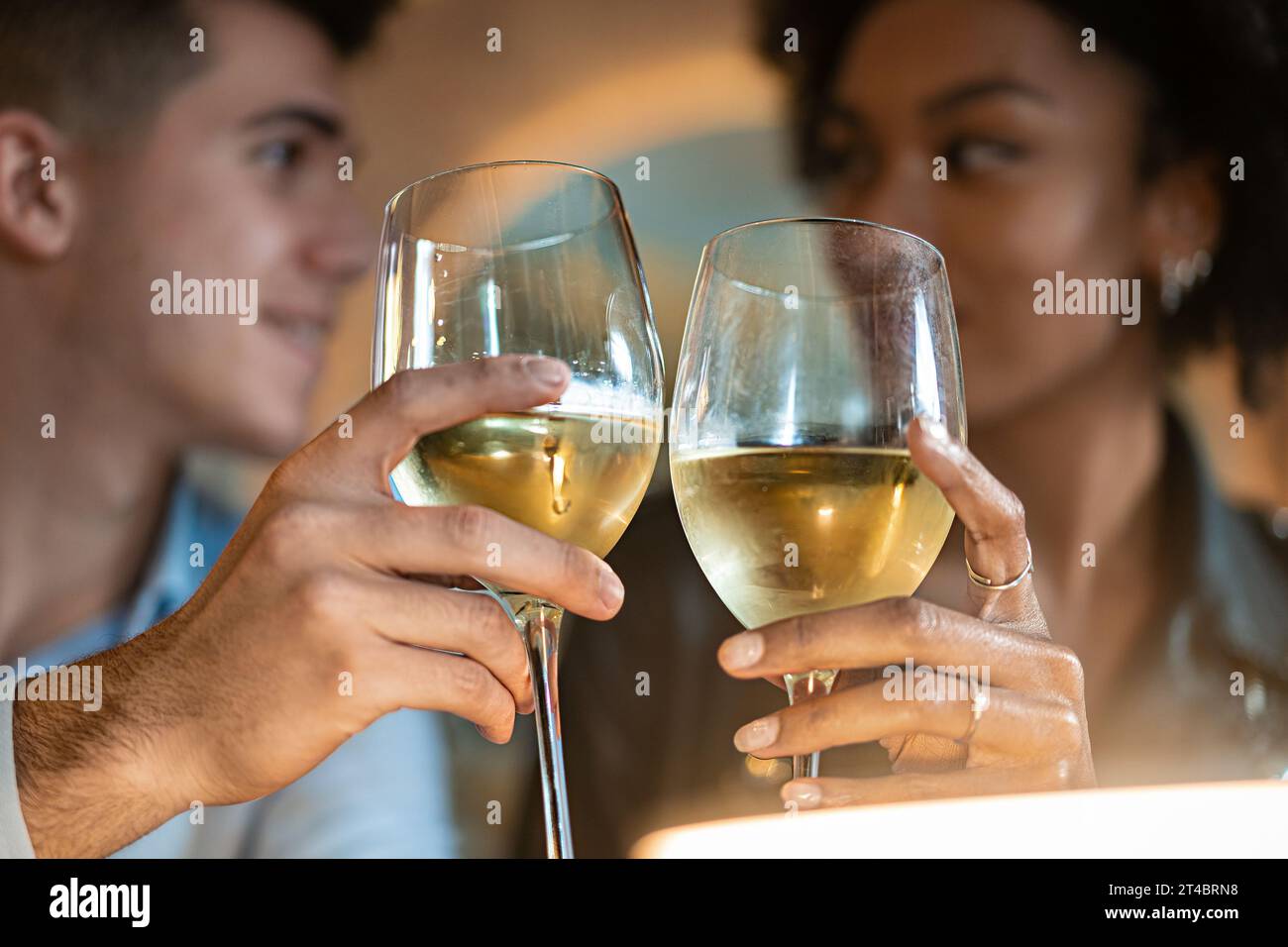 An intimate close-up of a young man and woman toasting with glasses of white wine. Their focused expressions and the clink of glasses symbolize celebr Stock Photo