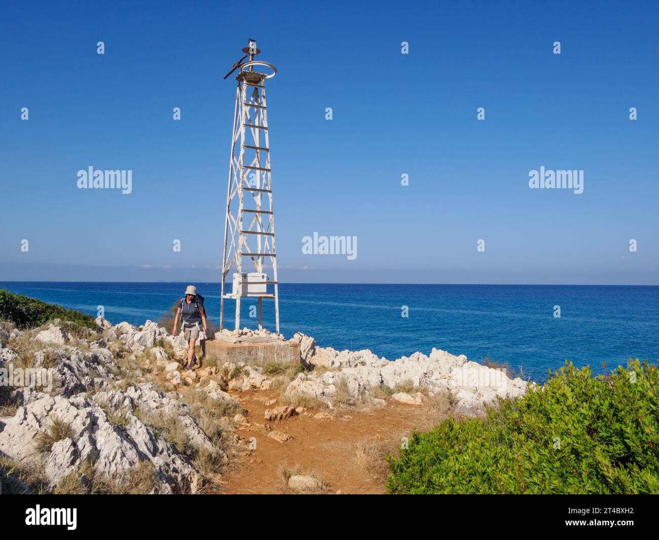 Walker rounding rocky Cape Agia Ekatarinis the most northerly point of Corfu with its small light beacon - Ionian Islands Greece Stock Photo