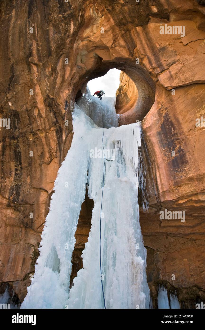 A man ice climbing a frozen waterfall through a sandstone arch in Utah. Stock Photo