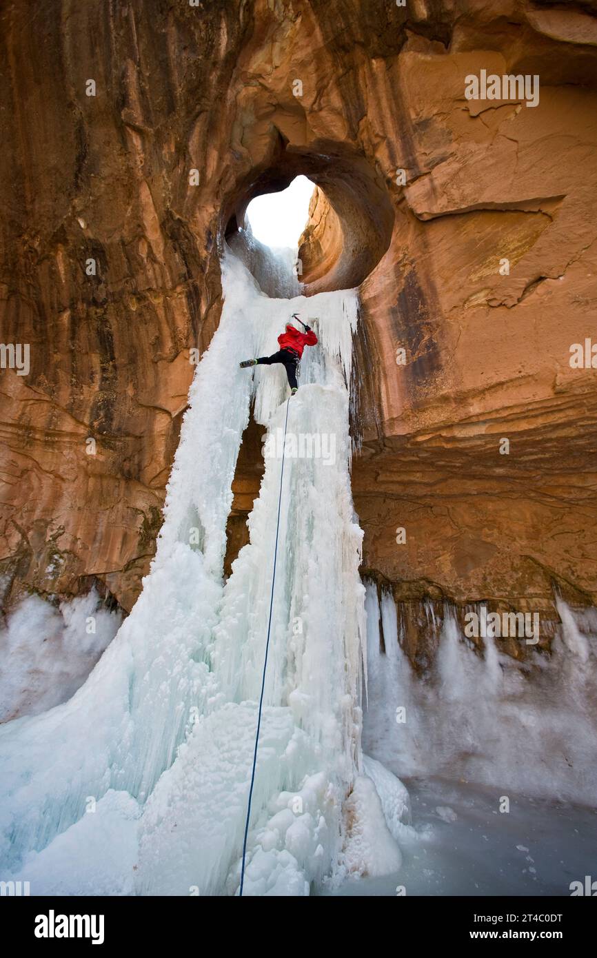 A man ice climbing a frozen waterfall through a sandstone arch in Utah. Stock Photo