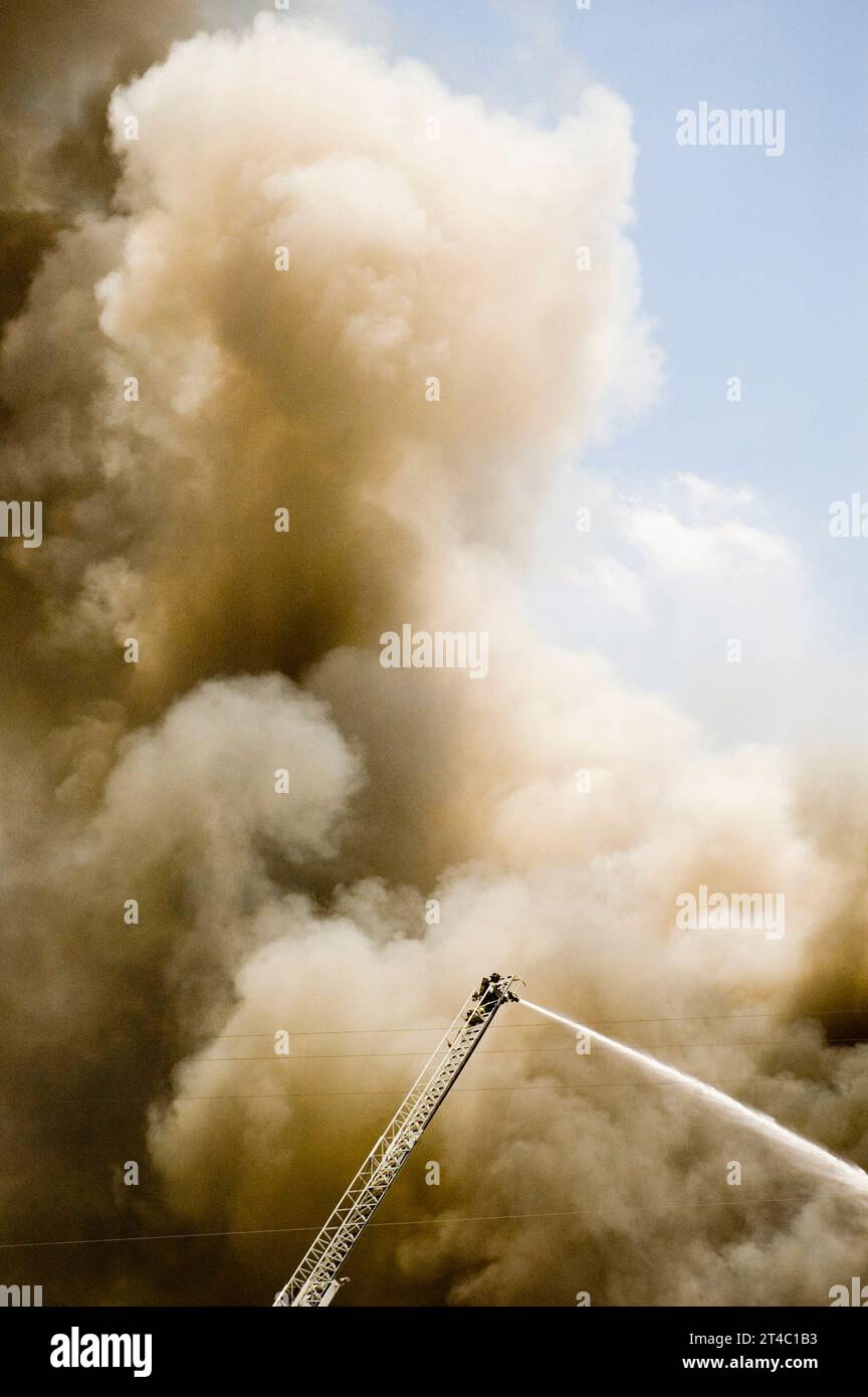 A firefighter sprays water from his ladder high above flames. Stock Photo