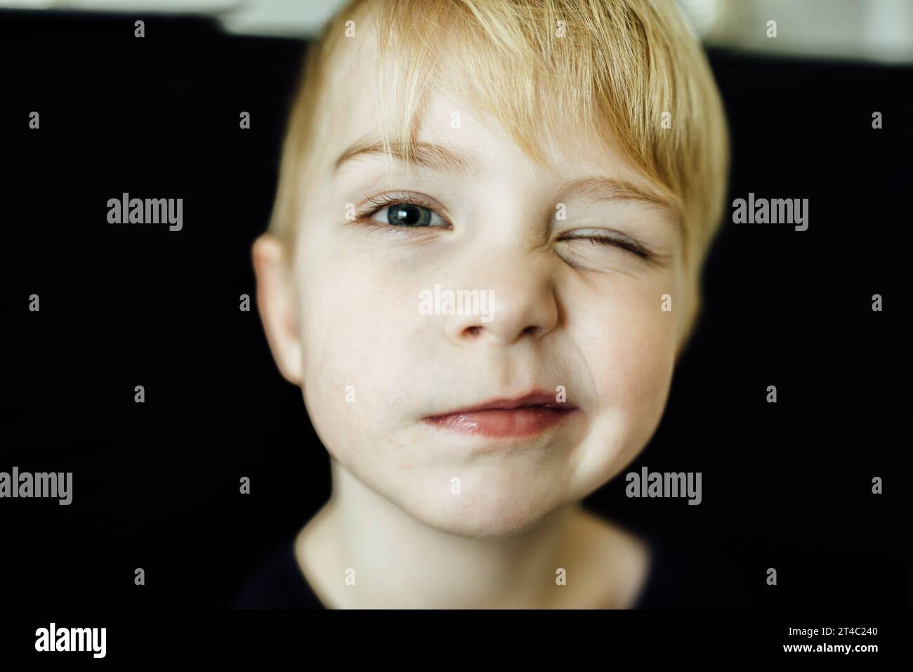 Young boy winks with goofy face at camera with black background Stock Photo