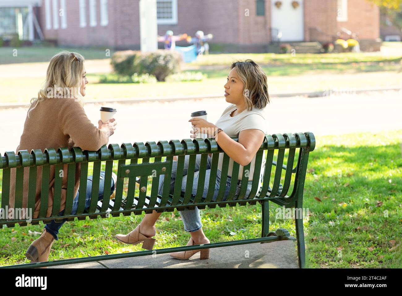 Two women sitting on bench drinking coffee and talking Stock Photo