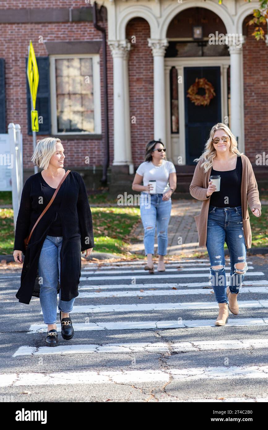 three women walking across the street on a crosswalk Stock Photo