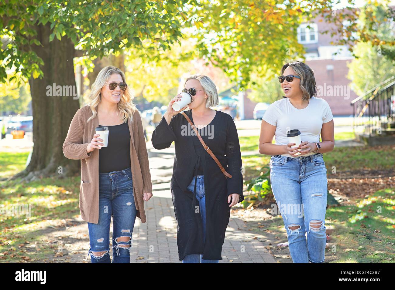 Three women walking down Main Street drinking coffee; friendship Stock Photo