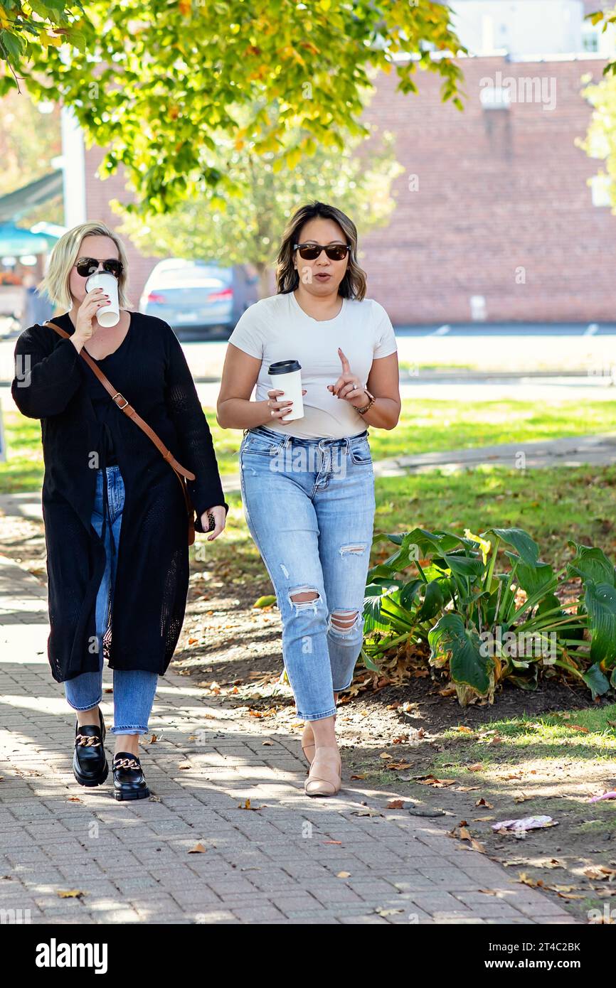 Two women in their 30s walking outside talking, drinking coffee Stock Photo