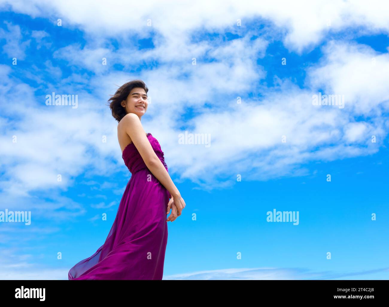 Teen girl in purple dress standing against blue skies Stock Photo