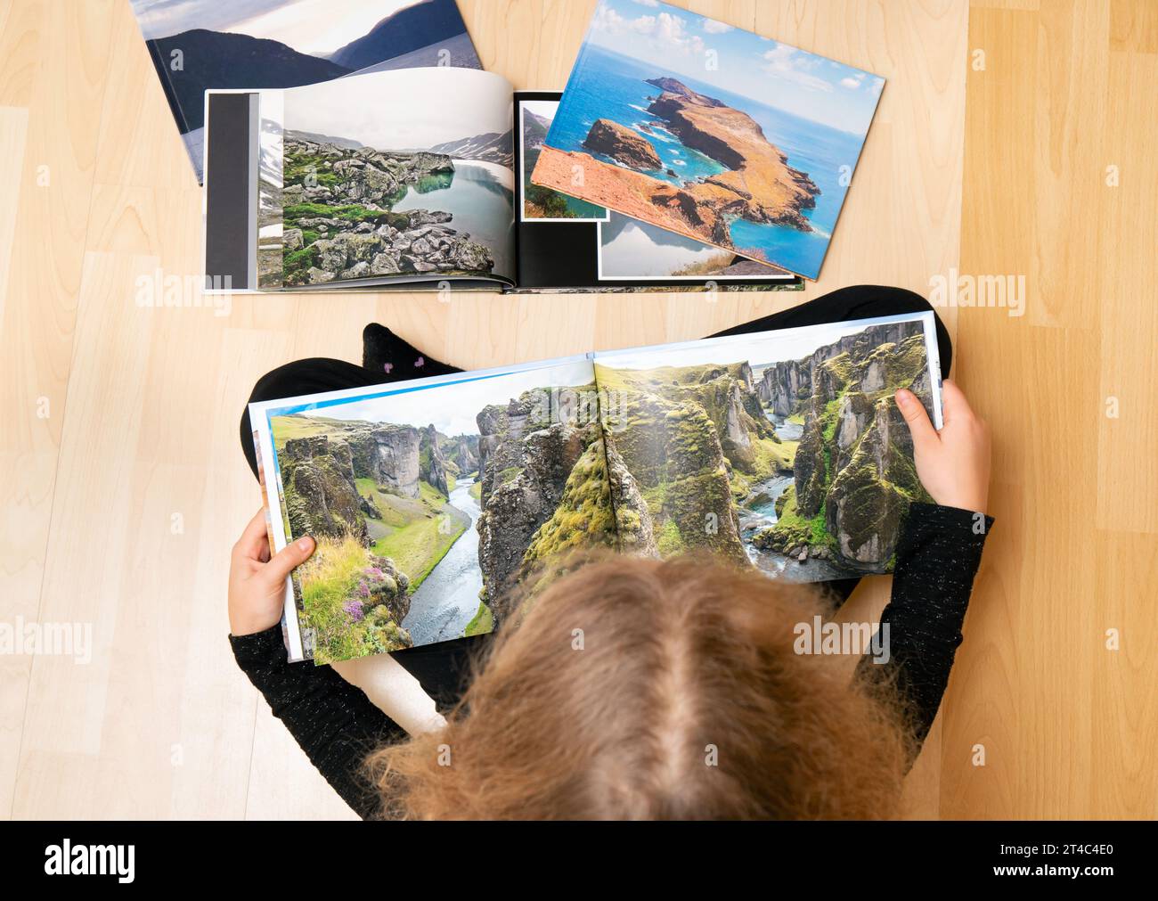 Child looking at the printed real paper travel photo books on home floor. Photographer has copyrights of the pictures in books, they are handmade. Stock Photo