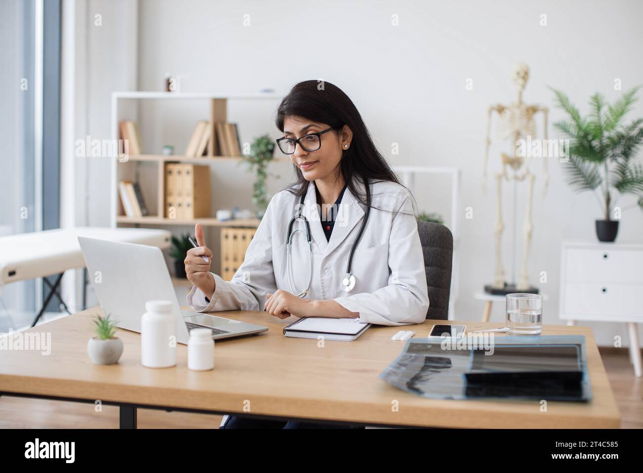 Competent doctor using modern laptop and gesturing during online video consultation. Indian woman in medical uniform telling about home treatment plan Stock Photo