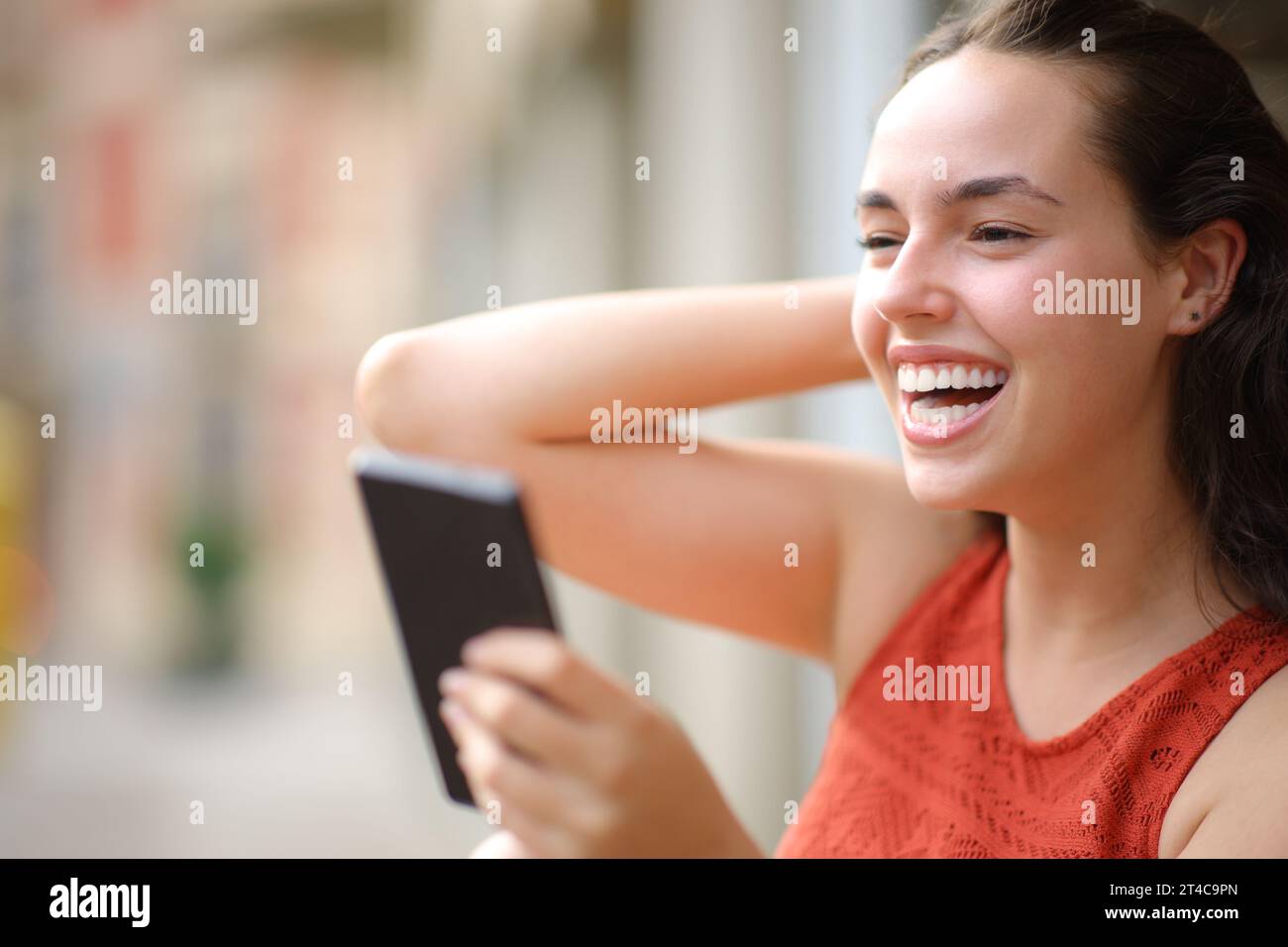 Happy woman laughing holding smartphone looking away in the street Stock Photo