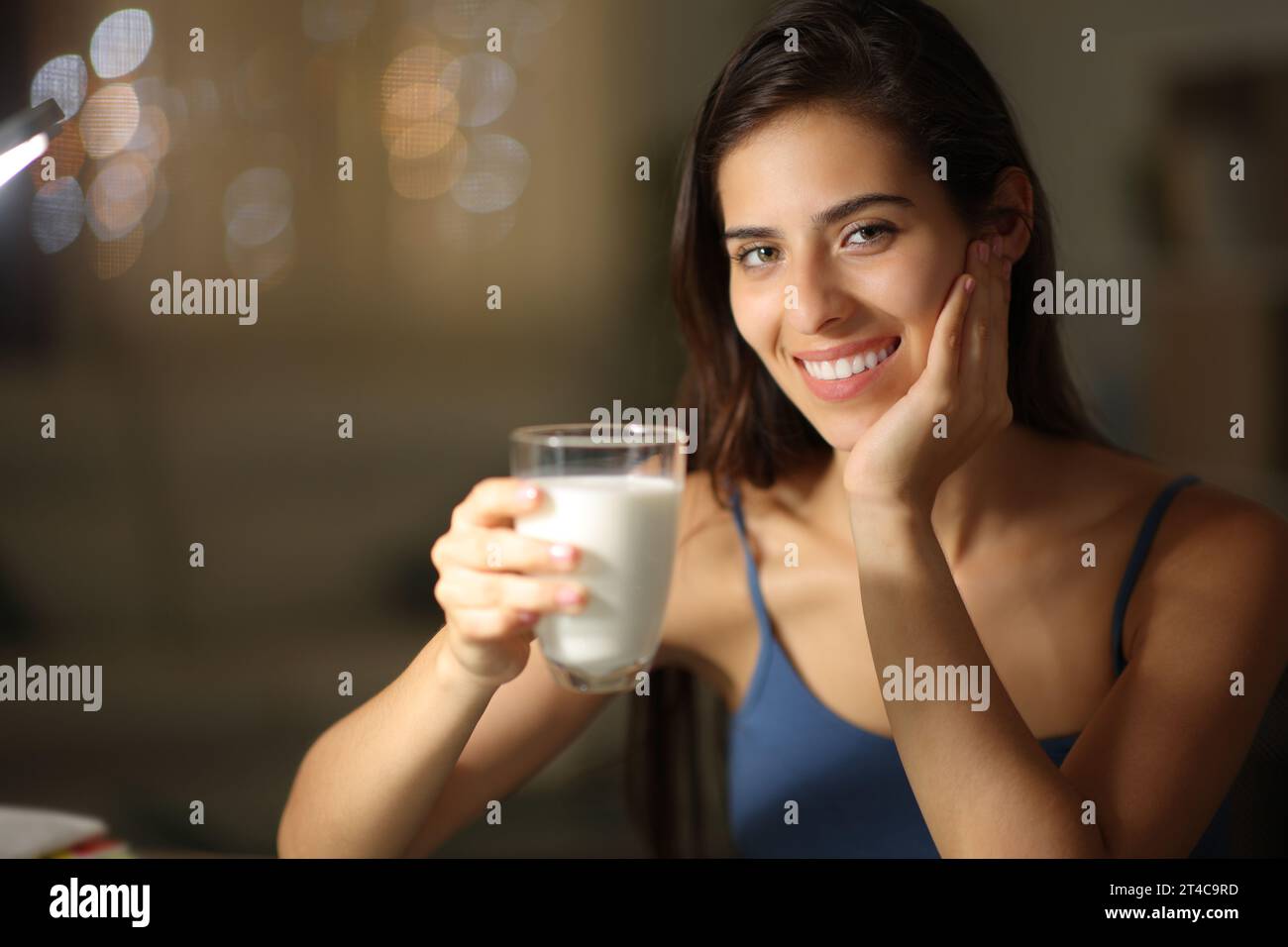 Happy woman in the night holding milk glass at home looking at you Stock Photo