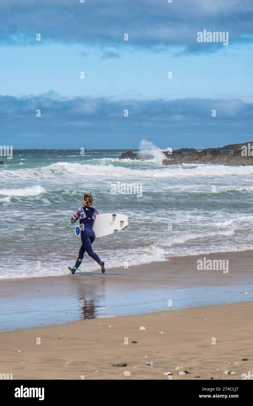 A keen enthusiastic female surfer carrying her surfboard and running into the sea at Fistral in Newquay in Cornwall in the UK. Stock Photo