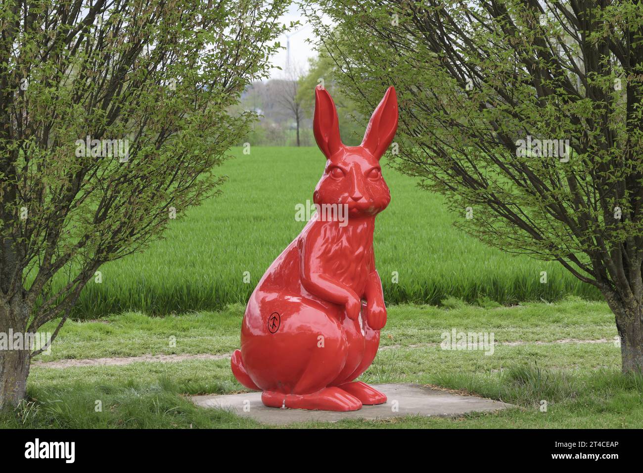 Tree Shaping Rabbit Red sculpture rabbit between trees in front of grain field , Germany ...